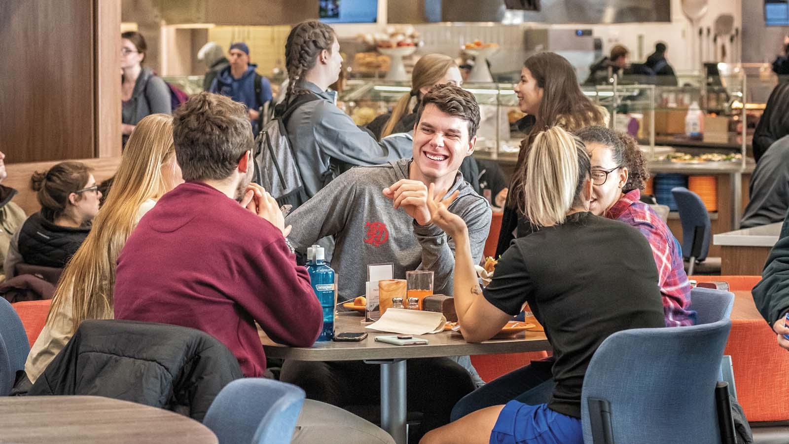 Group of students eating a meal together and laughing in the Crow’s Nest Campus Restaurant